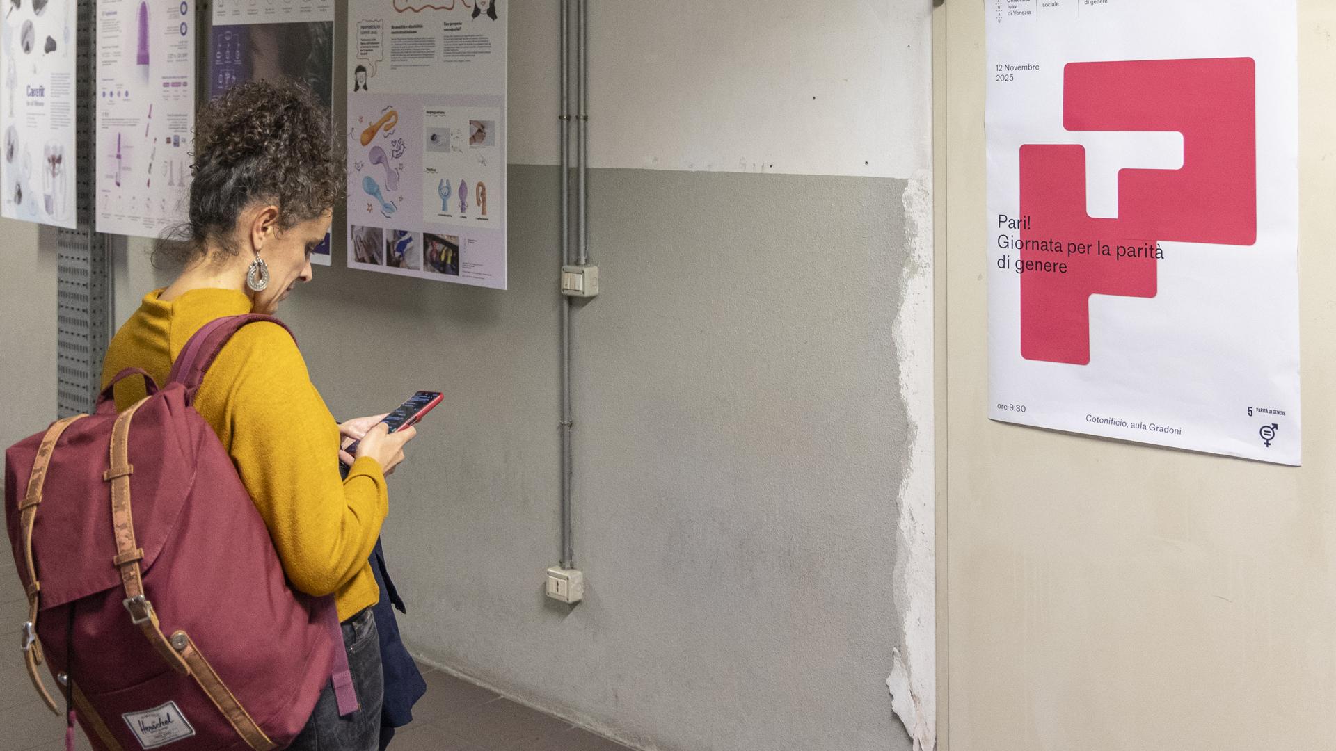 Ragazza con zaino e maglione giallo di fronte al poster dell'edizione 2025 della giornata per la parità di genere